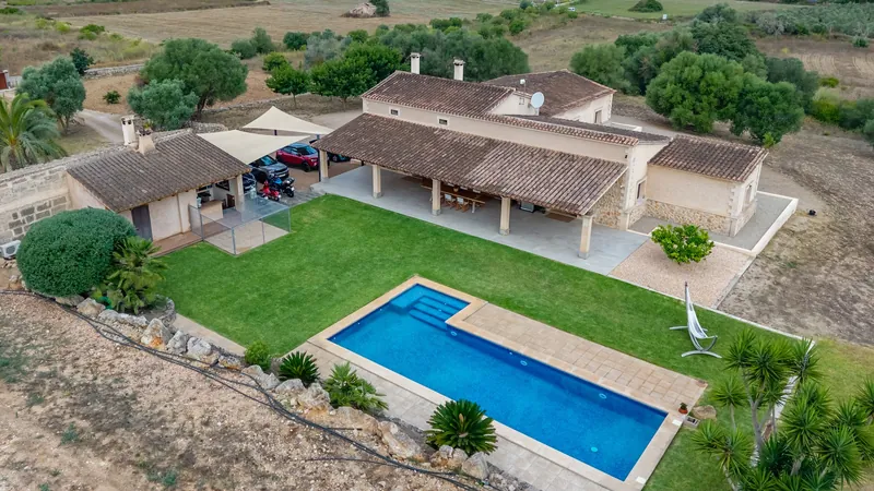 Casa de campo con césped y piscina rodeada de árboles, desde el dron