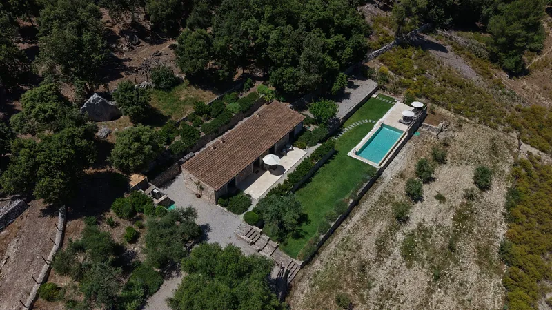 Edificio de piedra de un hotel rural con jardín y piscina alargada desde el aire