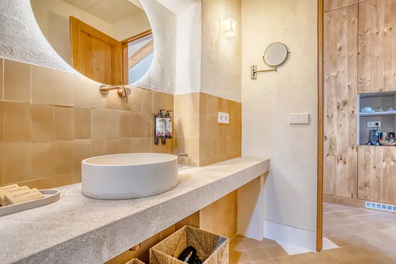 Baño con encimera de piedra, lavabo de cerámica y espejo de formas orgánicas
