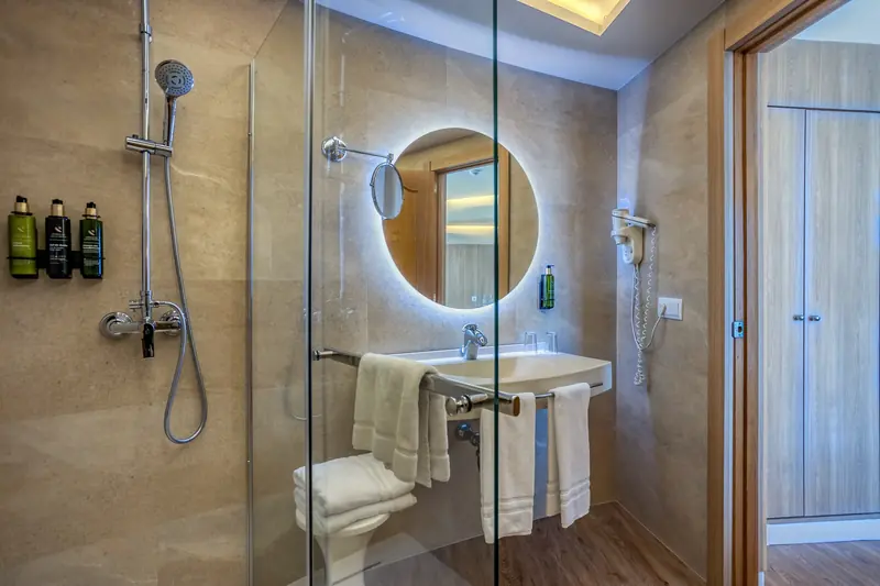 Baño de habitación de hotel con ducha de obra y espejo redondo iluminado