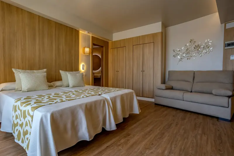 Habitación de hotel con dos camas, armario de madera y sofá