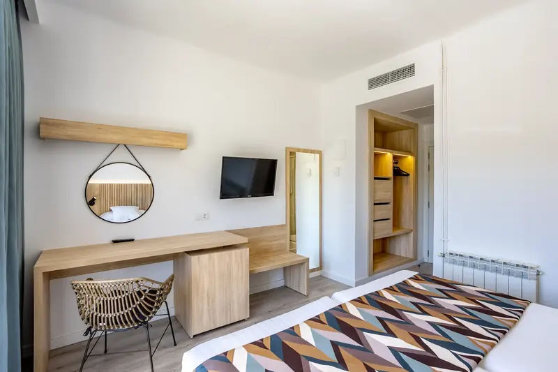 Habitación de hotel con escritorio de madera, espejo redondo y televisor