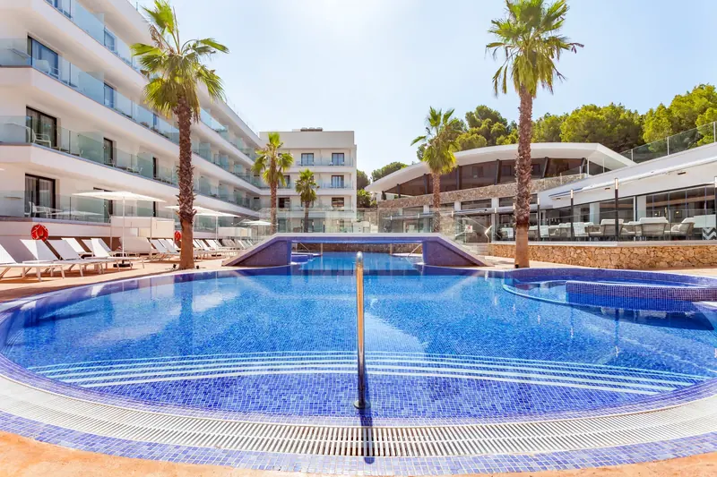Piscina de hotel rodeada de palmeras y edificios con terrazas