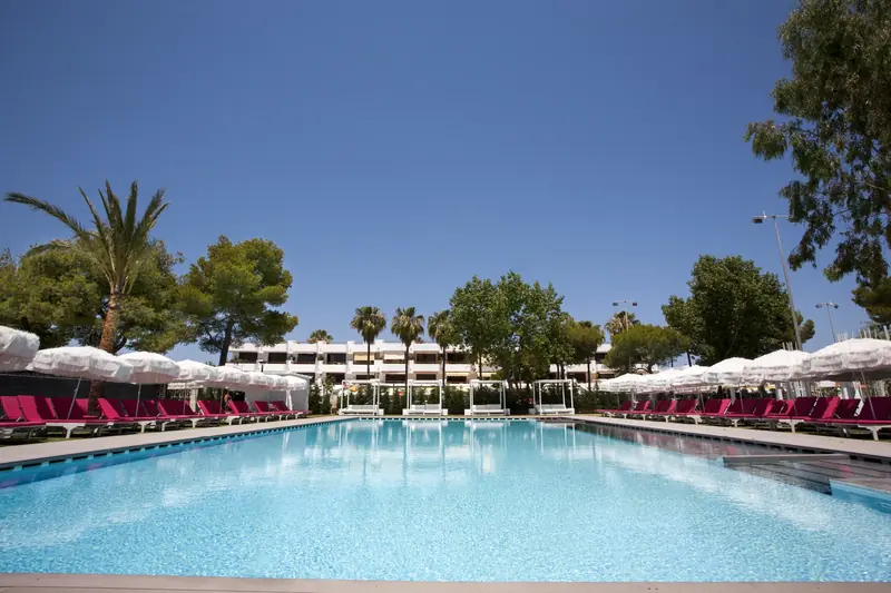 Piscina de hotel con sombrillas junto a un pinar