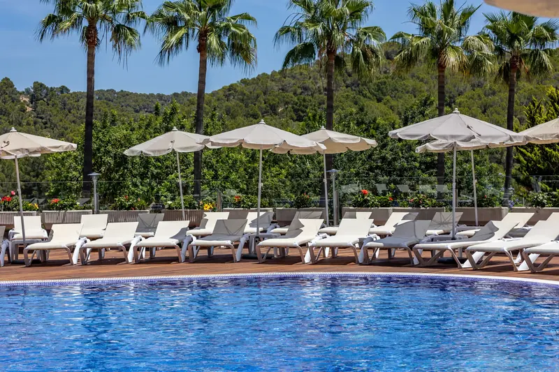 Piscina de hotel con hilera de tumbonas y sombrillas bajo las palmeras