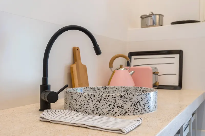 Detalle de cocina con grifo negro y fregadero de terrazo