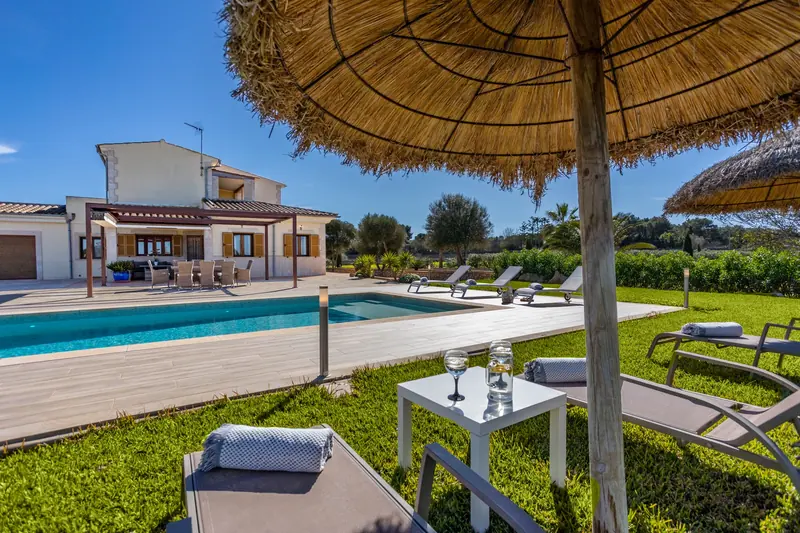 Jardín con piscina, tumbonas y sombrilla de paja
